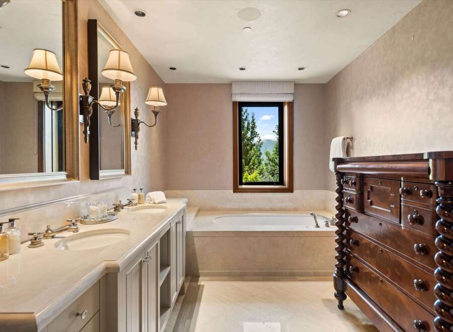 Indulge in luxury with this stunning bathroom featuring a spacious double vanity with marble countertops and elegant sconce lighting.