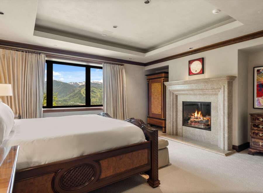Experience luxury mountain living in this exquisite bedroom, featuring a grand fireplace and breathtaking panoramic views of snow-capped peaks.