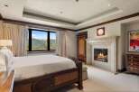 Experience luxury mountain living in this exquisite bedroom, featuring a grand fireplace and breathtaking panoramic views of snow-capped peaks.