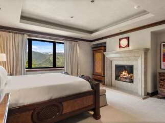 Experience luxury mountain living in this exquisite bedroom, featuring a grand fireplace and breathtaking panoramic views of snow-capped peaks.