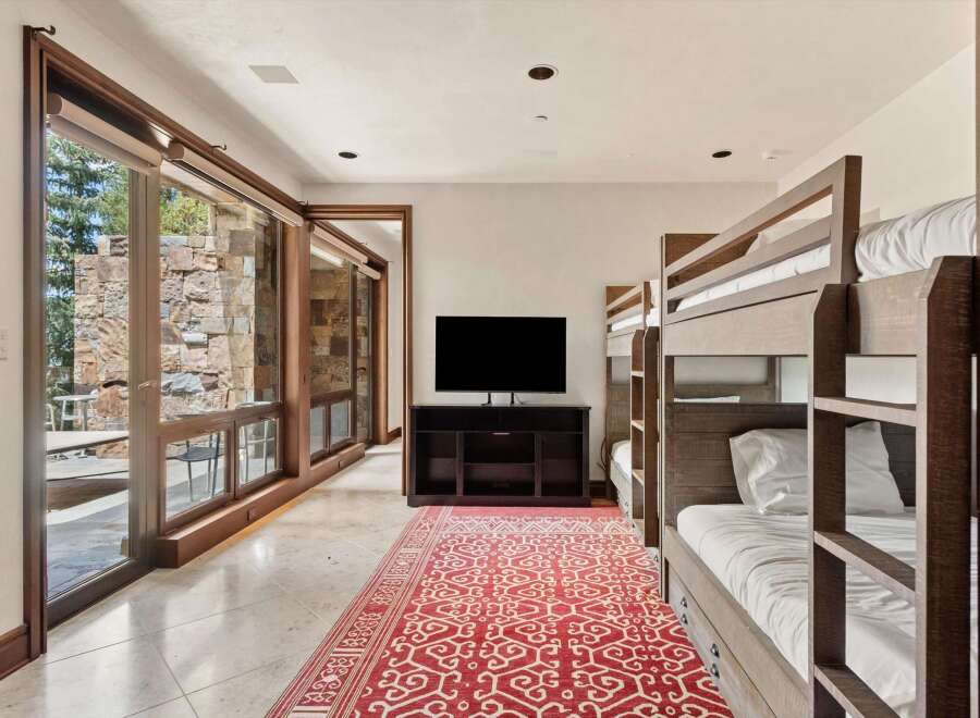 This spacious room features a modern entertainment area with a large flat-screen TV and a dark wood media console, complemented by a vibrant red and white patterned rug.