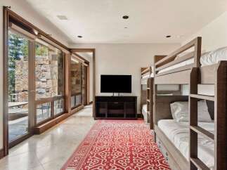 This spacious room features a modern entertainment area with a large flat-screen TV and a dark wood media console, complemented by a vibrant red and white patterned rug.