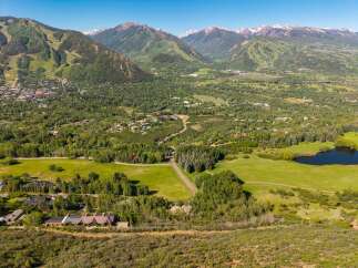 Experience luxury mountain living with this stunning aerial view of a sprawling estate nestled amidst lush greenery and majestic peaks.