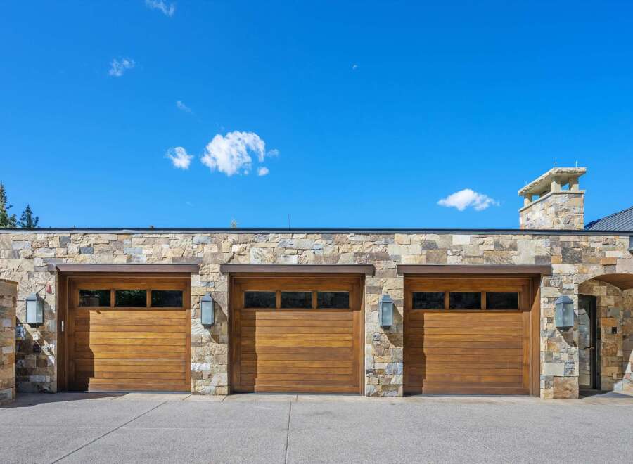This stunning property boasts a grand facade featuring three expansive wooden garage doors, complemented by a rustic stone exterior.