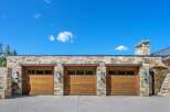 This stunning property boasts a grand facade featuring three expansive wooden garage doors, complemented by a rustic stone exterior.