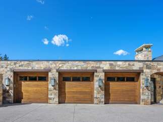 This stunning property boasts a grand facade featuring three expansive wooden garage doors, complemented by a rustic stone exterior.