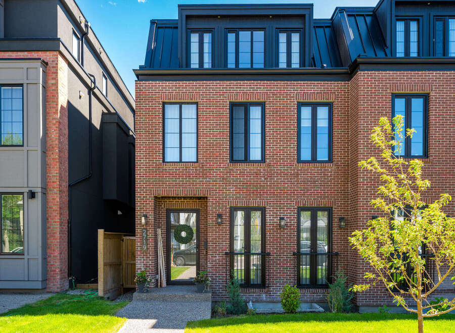 Discover modern urban living in this stunning brick townhouse, featuring a sleek black metal roof and expansive windows for abundant natural light.