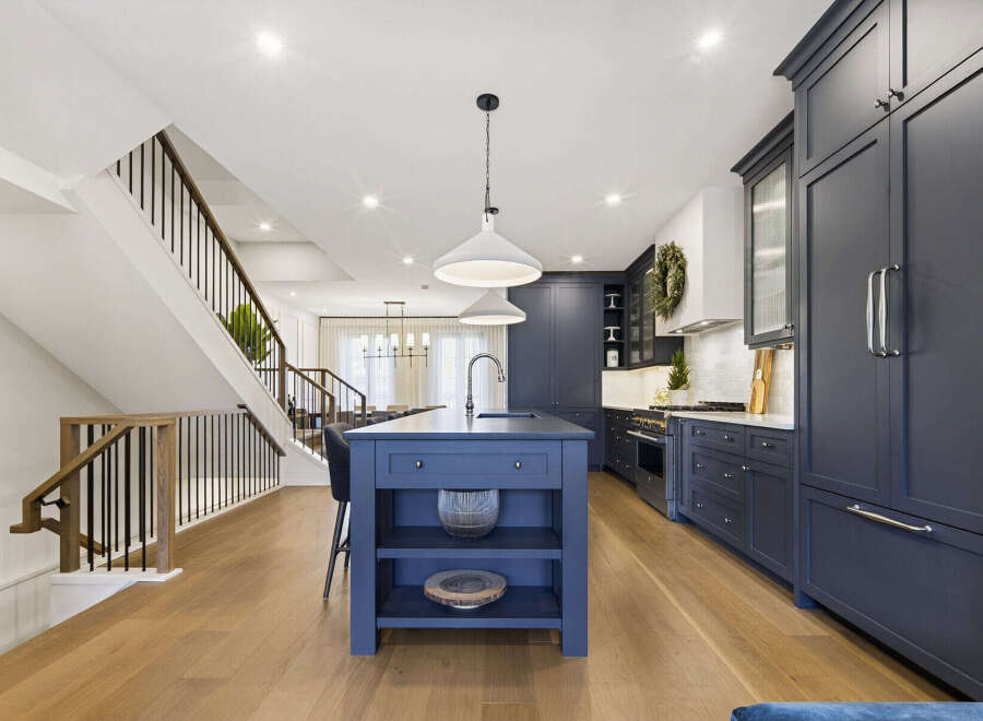 Experience luxury living in this stunning modern kitchen, featuring a spacious navy blue island with a waterfall countertop and sleek pendant lighting.