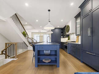 Experience luxury living in this stunning modern kitchen, featuring a spacious navy blue island with a waterfall countertop and sleek pendant lighting.