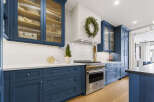 Experience culinary excellence in this stunning chef's kitchen, featuring deep navy custom cabinetry and a professional-grade stainless steel range.