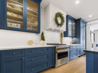 Experience culinary excellence in this stunning chef's kitchen, featuring deep navy custom cabinetry and a professional-grade stainless steel range.