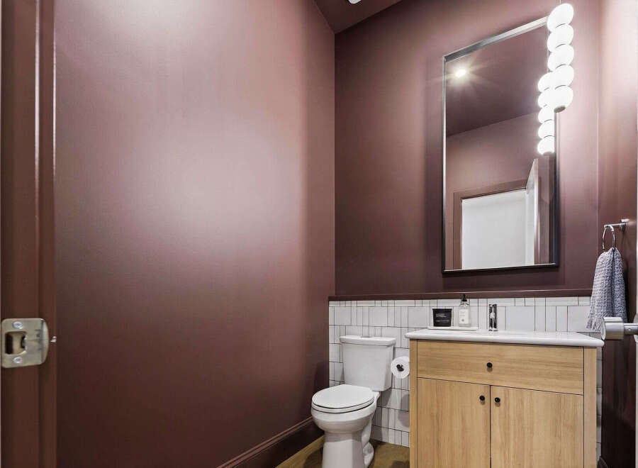 This modern powder room features a deep plum accent wall, complemented by a sleek vanity with a light wood finish and a white countertop.