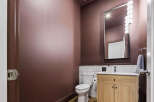 This modern powder room features a deep plum accent wall, complemented by a sleek vanity with a light wood finish and a white countertop.