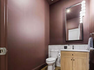 This modern powder room features a deep plum accent wall, complemented by a sleek vanity with a light wood finish and a white countertop.