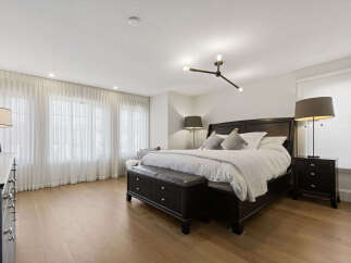 Experience ultimate comfort in this luxurious master bedroom, featuring a spacious king-size bed adorned with plush white linens and elegant throw pillows.