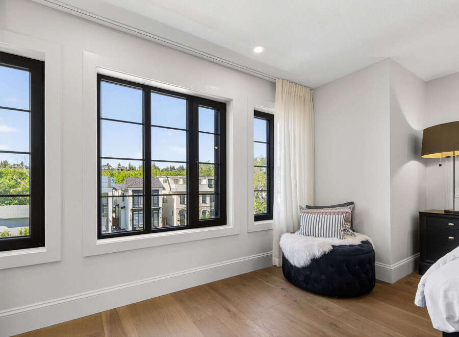 Experience luxury living in this beautifully appointed bedroom featuring expansive black-framed windows that offer picturesque views of the surrounding neighborhood.