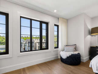 Experience luxury living in this beautifully appointed bedroom featuring expansive black-framed windows that offer picturesque views of the surrounding neighborhood.