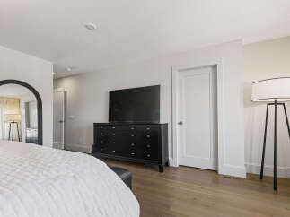 Experience modern comfort in this spacious bedroom, featuring a sleek black dresser topped with a large flat-screen TV and a striking arched mirror.