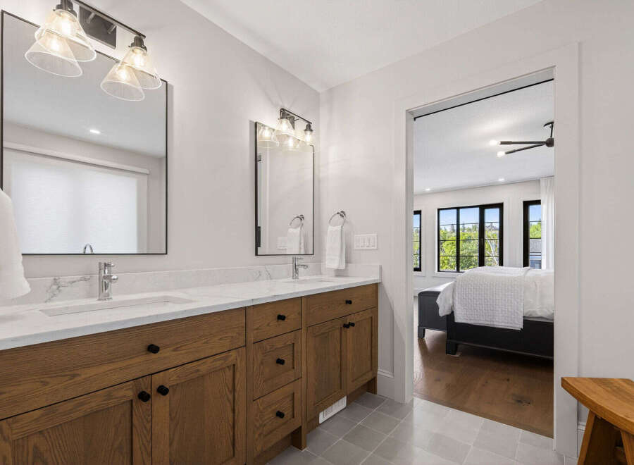 This modern bathroom features a spacious double vanity with sleek wooden cabinetry and marble countertops, complemented by elegant glass pendant lighting.