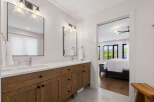 This modern bathroom features a spacious double vanity with sleek wooden cabinetry and marble countertops, complemented by elegant glass pendant lighting.