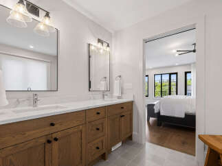 This modern bathroom features a spacious double vanity with sleek wooden cabinetry and marble countertops, complemented by elegant glass pendant lighting.
