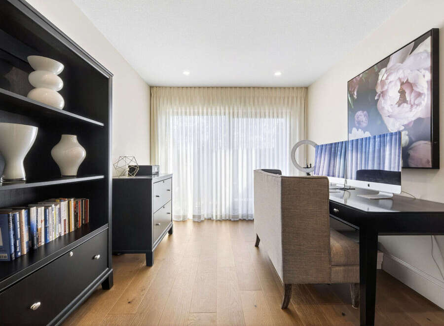 This home office features a sleek black bookshelf filled with decor and books, complemented by a modern black dresser.