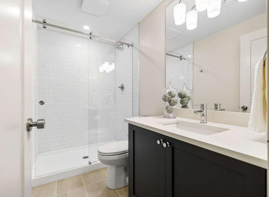This modern bathroom features a sleek glass-enclosed shower with white subway tiles and a rainfall showerhead.