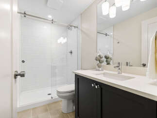 This modern bathroom features a sleek glass-enclosed shower with white subway tiles and a rainfall showerhead.