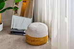 Enhance your living space with this charming, two-toned woven ottoman, featuring a natural jute base and a soft white top.