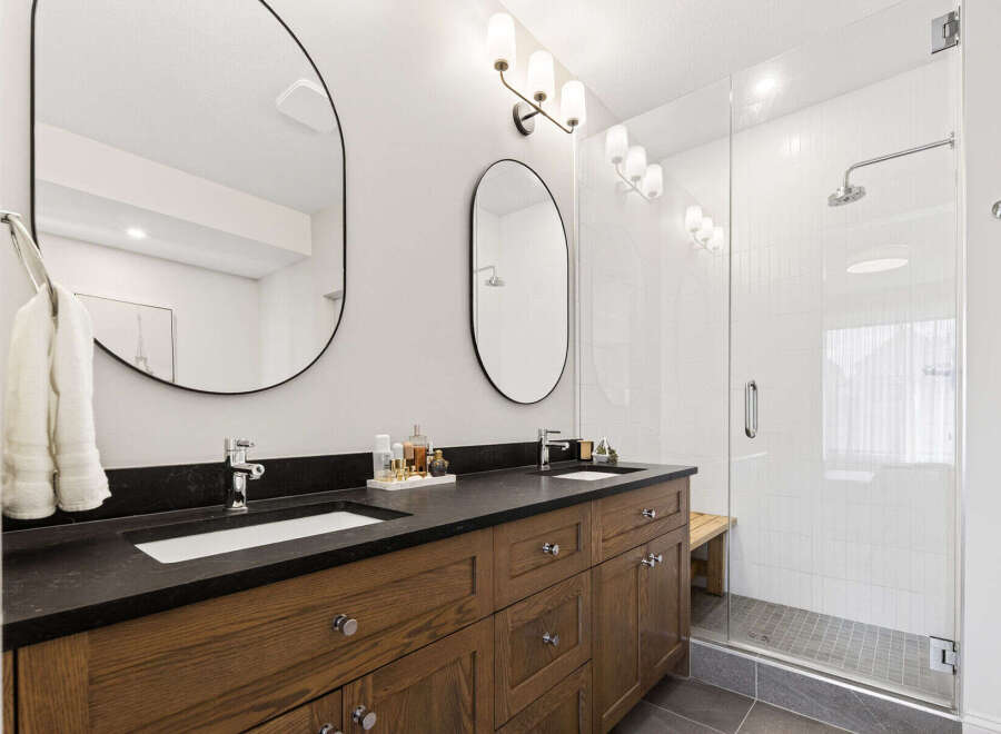 Experience modern luxury in this stunning bathroom featuring a spacious double vanity with sleek black countertops and warm wood cabinetry.