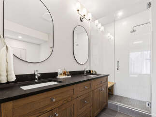 Experience modern luxury in this stunning bathroom featuring a spacious double vanity with sleek black countertops and warm wood cabinetry.
