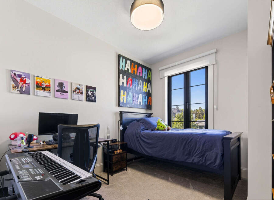 This modern bedroom features a comfortable bed with navy blue bedding, a spacious desk with a computer and keyboard, and vibrant wall art.