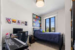 This modern bedroom features a comfortable bed with navy blue bedding, a spacious desk with a computer and keyboard, and vibrant wall art.