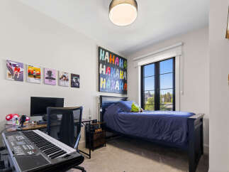 This modern bedroom features a comfortable bed with navy blue bedding, a spacious desk with a computer and keyboard, and vibrant wall art.