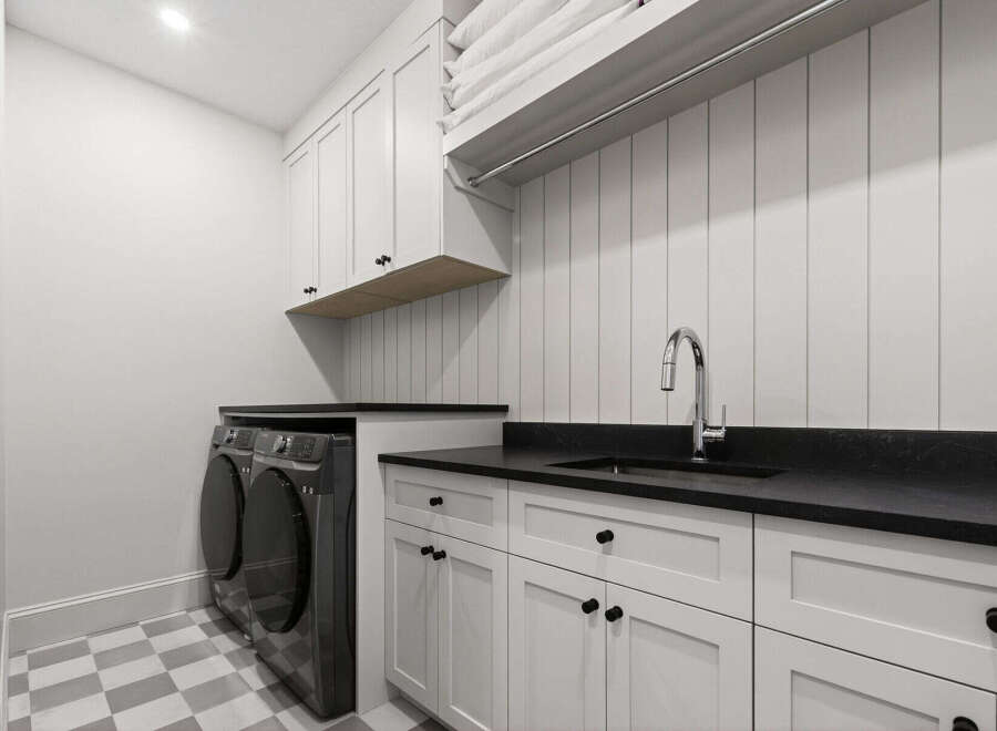 This modern laundry room features a sleek design with white shaker cabinets and a black countertop.