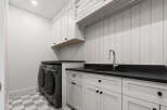 This modern laundry room features a sleek design with white shaker cabinets and a black countertop.
