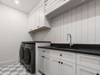 This modern laundry room features a sleek design with white shaker cabinets and a black countertop.