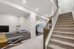 Discover modern living with this spacious basement featuring a comfortable grey sectional sofa and a dedicated home gym enclosed by sleek glass walls.