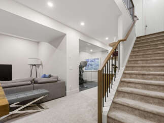 Discover modern living with this spacious basement featuring a comfortable grey sectional sofa and a dedicated home gym enclosed by sleek glass walls.