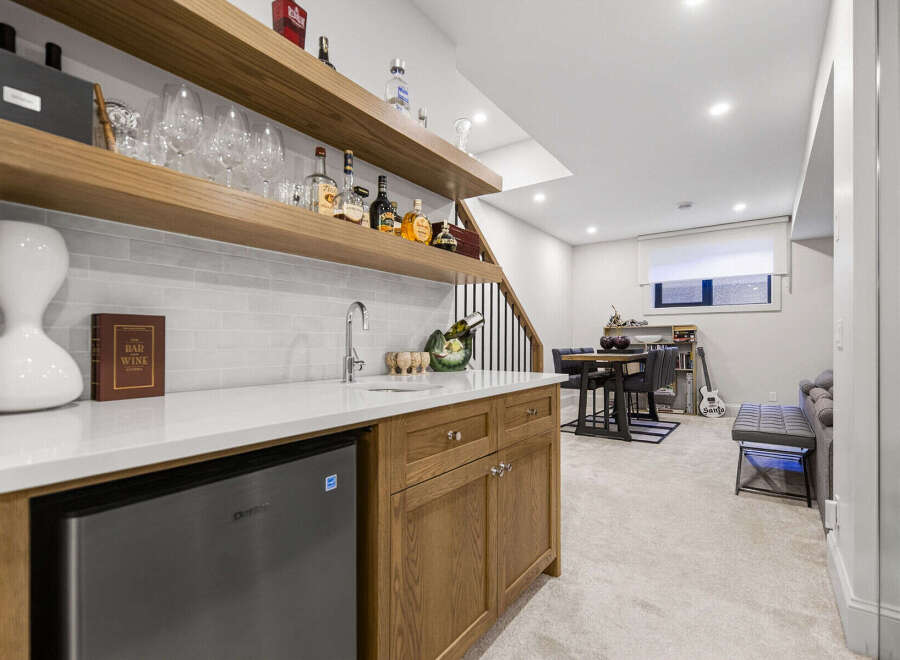 This modern basement features a stylish wet bar with a built-in mini-fridge and ample shelving for glassware and spirits.