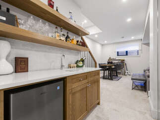 This modern basement features a stylish wet bar with a built-in mini-fridge and ample shelving for glassware and spirits.