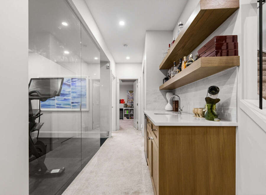 This modern home features a stylish wet bar with floating wooden shelves, a sleek white countertop, and a contemporary sink, perfect for entertaining.