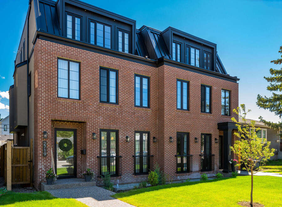 Discover modern luxury in this stunning brick townhouse featuring a sleek black metal roof and expansive windows.