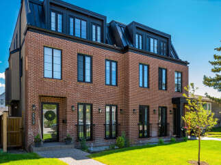 Discover modern luxury in this stunning brick townhouse featuring a sleek black metal roof and expansive windows.