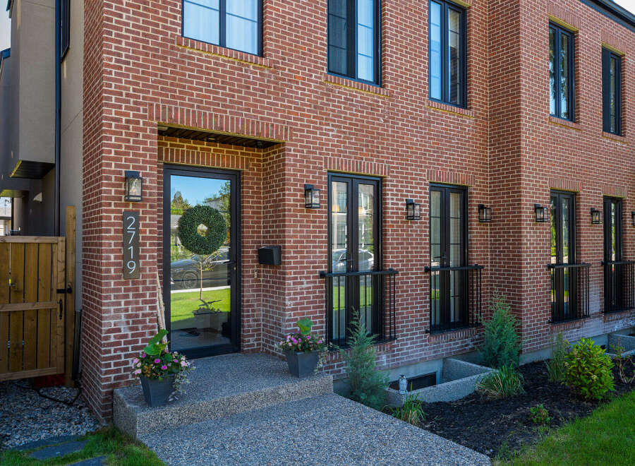 Discover modern living in this stunning red brick townhouse, featuring sleek black window frames and a welcoming front entrance with a festive wreath.