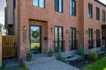 Discover modern living in this stunning red brick townhouse, featuring sleek black window frames and a welcoming front entrance with a festive wreath.