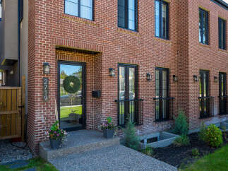 Discover modern living in this stunning red brick townhouse, featuring sleek black window frames and a welcoming front entrance with a festive wreath.