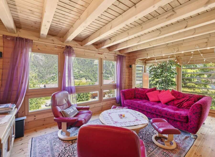 Experience cozy living in this charming log cabin living room, featuring a vibrant floral sofa and plush red armchairs perfect for relaxation.