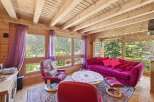 Experience cozy living in this charming log cabin living room, featuring a vibrant floral sofa and plush red armchairs perfect for relaxation.