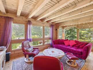 Experience cozy living in this charming log cabin living room, featuring a vibrant floral sofa and plush red armchairs perfect for relaxation.